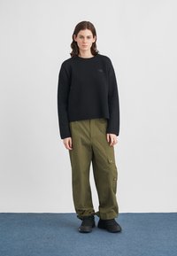 Μαύρο cropped πουλόβερ με μακριά μανίκια, σε συνδυασμό με χακί cargo παντελόνια με τσέπες και κουμπώματα. Μαύρα παπούτσια ολοκληρώνουν το σύνολο.