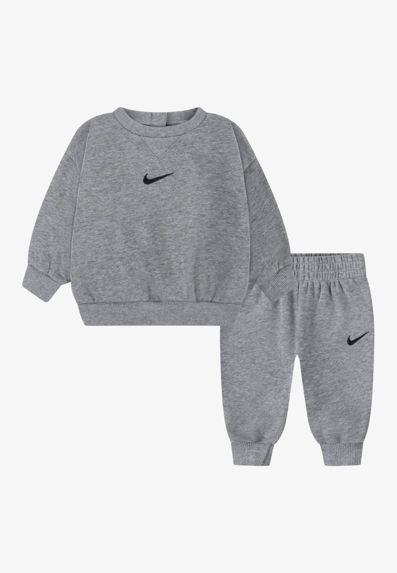Pilkas džemperis ir kelnių komplektas, pagamintas iš minkštos medžiagos. Turintis gūžtinės rankoves ir mažą juodą Nike logotipą abiejuose drabužiuose. Kasdienis dizainas.