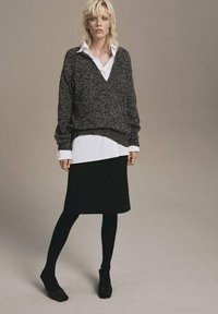 Outfit in bianco e nero composto da un maglione grigio oversize con texture indossato sopra una camicia bianca, abbinato a una gonna nera lunga fino al ginocchio e collant neri.