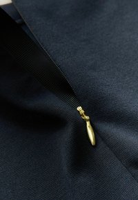Tissu bleu marine foncé avec une fermeture éclair visible dotée d'un tirette en ton doré, présentant une texture lisse et un design épuré.