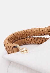Vit handväska med en strukturerad yta och triangulär klaff, prydd med ett beige flätat handtag och ett detaljer i guld.