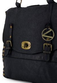 Sort lærertaske med klaplås, hardware i messing, nittebesætning på siden og et rundt mærke. Har tekstureret overflade og justerbar rem.