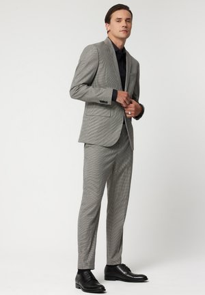 Grå rutigt kostym med slim fit, texturerad tyg, snedskurna slag och framfickor. Kombineras med svarta finskor och en svart skjorta.