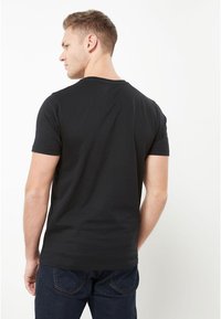 Svart bomullströja med korta ärmar, rund halsringning, mjuk textur, figurnära passform, sedd bakifrån, tillsammans med mörka denimjeans.