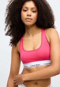 Ροδοκόκκινο βαμβακερό bralette με τετράγωνη λαιμόκοψη και λεπτές τιράντες. Διαθέτει λευκή ελαστική ζώνη με μαύρο κείμενο "Calvin Klein" στο κάτω μέρος.