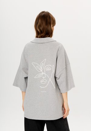 Grijze oversized shirt met korte mouwen, voorzien van een witte lijntekening van een gezicht en een bladontwerp op de achterkant. Zachte stof, ontspannen pasvorm.