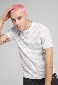 Hvid kortærmet t-shirt med gentaget sort teksttrykt. Har en rund halsudskæring og en afslappet pasform, parret med mørk denim jeans.