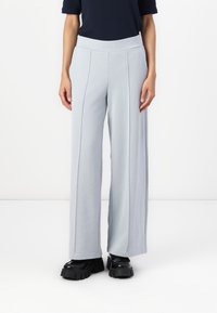 Ανοιχτό γκρι παντελόνι φαρδιάς γραμμής με ψηλή ελαστική μέση. Ο ύφασμα φαίνεται μαλακό και ρέει. Φοράει χοντρές μαύρες πλατφόρμες.