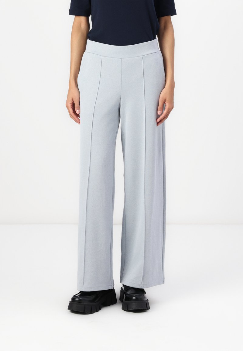 Ανοιχτό γκρι παντελόνι φαρδιάς γραμμής με ψηλή ελαστική μέση. Ο ύφασμα φαίνεται μαλακό και ρέει. Φοράει χοντρές μαύρες πλατφόρμες.