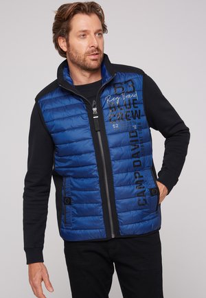 Gilet imbottito blu con maniche nere, zip frontale e tasche laterali. Presenta testo in rilievo e una morbida texture trapuntata.