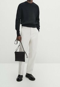 Black ribbed sweater, white tailored trousers, black leather shoes, and a small black bag with a strap. Minimalist and modern design.