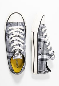 Baskets en toile à motif pied-de-poule noir et blanc, avec des lacets blancs, un embout en caoutchouc et un intérieur jaune. Bord de semelle rayé noir.