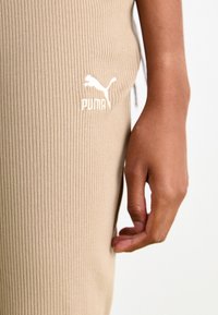 Leggings de tela acanalada beige con un diseño ajustado, que cuentan con un logotipo bordado en blanco de Puma en el muslo y una textura suave.