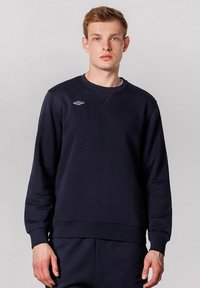 Felpa navy con collo rotondo, polsini e orlo a costine, realizzata in tessuto morbido, con un piccolo logo bianco sul petto.