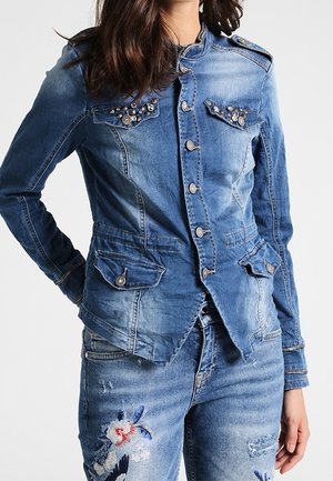 Giubbotto di jeans con una forma classica, colore blu chiaro, due tasche sul petto con decorazioni e chiusure a bottoni metallici.