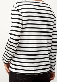 Maglietta a righe bianche e nere a maniche lunghe con scollo rotondo e vestibilità rilassata, caratterizzata da un orlo curvo e una morbida texture di cotone.