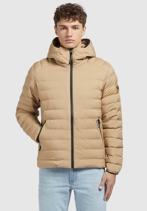 Beige vadderad jacka med dragkedja fram, huva och elastiska ärmslut. Har svarta dragkedjefickor och en logo på vänster arm.