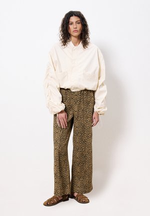 Chemise légère crème avec col montant et deux poches, associée à un pantalon évasé à imprimé léopard marron et des sandales à lanières marron.