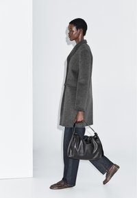 Grå uldfrakke med en skræddersyet pasform, parret med mørk denim jeans og brune loafers. Holder en sort læder skuldertaske.