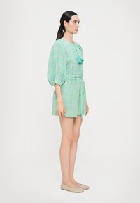 Zaļi un zili svītrainas īsām piedurknēm tērps ar pieguļošu vidukli un auklu. Iezīmē teksturētu audumu un mazu pušķi kakla izgriezumā.