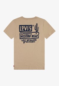 Camiseta de algodón beige con un diseño gráfico en azul marino que presenta el texto "LEVI'S", una ilustración de un cactus y las palabras "AUTÉNTICA ROPA DEL OESTE."