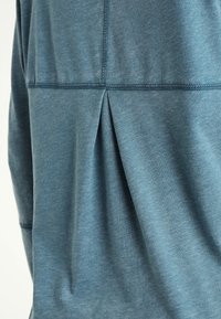 Niebieski, melanżowy top z długim rękawem, z plisą z tyłu, miękkim materiałem i kontrastującym przeszyciem. Lekka i oddychająca tkanina.