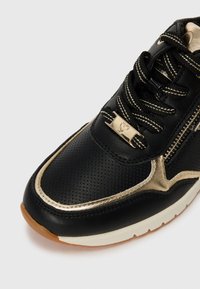 Black perforated leather sneaker with gold accents, featuring a rounded toe, contrast stitching, and a metallic heart detail on the lace.