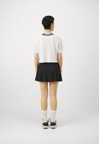 Tagatud valge T-särk musta triibulise kaelusega, mida kannab must lehvikseelik, valged sokid ja mustad tossud tagantvaates.