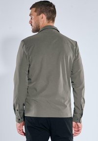 Olivgrünes Hemd mit Knopfleiste, glatter Textur, langen Ärmeln und Kragen. Verfügt über geknöpfte Manschetten und einen dezenten Rückenpasse.