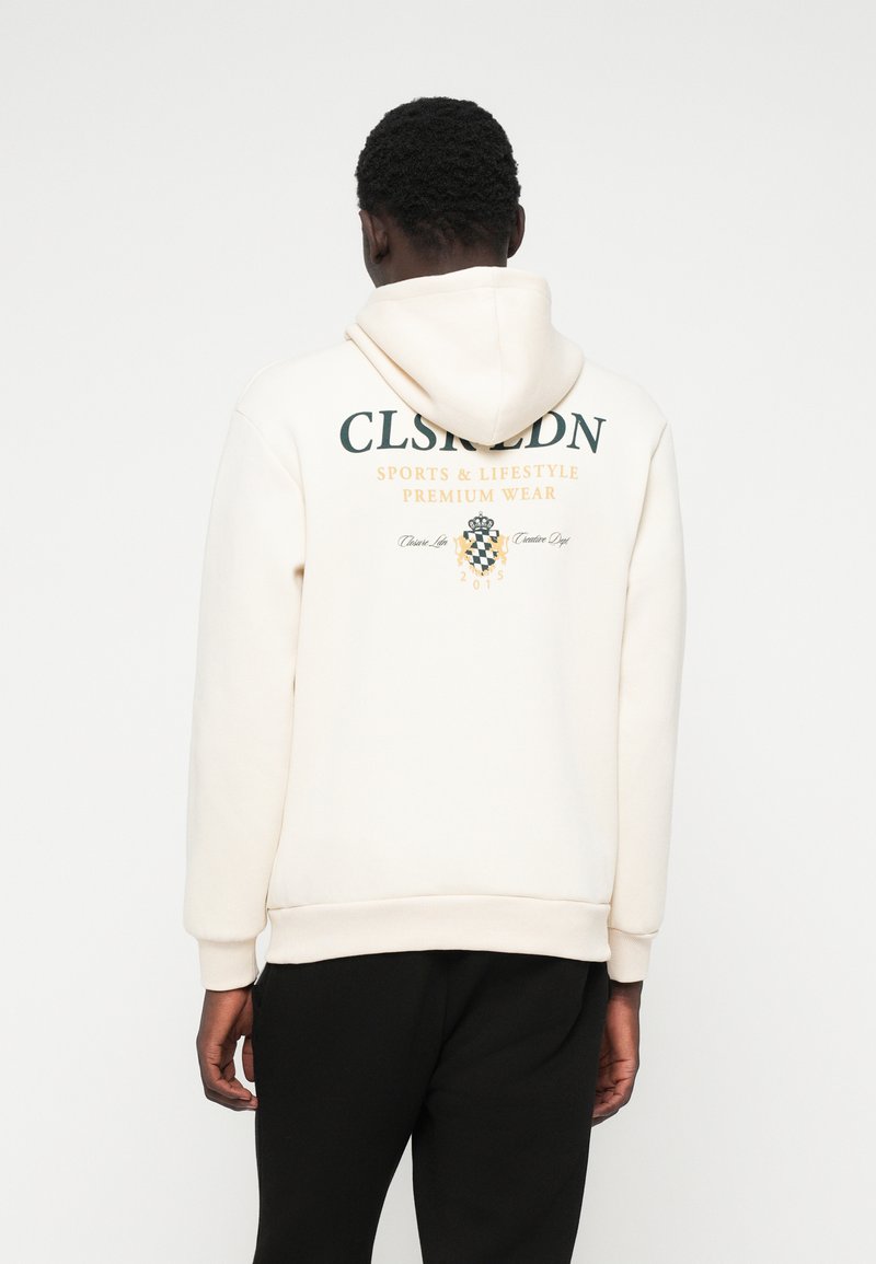 Κρέμα φούτερ με γραφικό σχέδιο στο πίσω μέρος σε πράσινο και πορτοκαλί, που διαθέτει το κείμενο "CLSRLDN SPORTS & LIFESTYLE PREMIUM WEAR". Μαλακό ύφασμα, άνετη εφαρμογή.