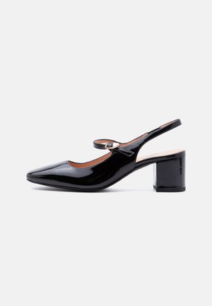 Scarpa slingback in pelle verniciata nera con tacco a blocco e fibbia a forma di cuore sulla fascia, mostrata di profilo su sfondo bianco.