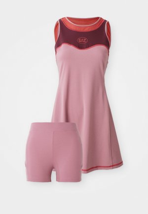 Top desportivo rosa com um detalhe e logótipo em maroon, combinado com calções rosa a condizer. Ambos os itens são feitos de um tecido liso e elástico.