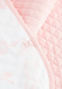Quilted pink fabric with a diamond pattern on one side and a soft, white cotton with light pink illustrations on the other, edged in pink trim.