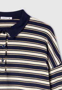 Polo a righe blu navy e panna con colletto, dotato di tre bottoni e una texture morbida. Etichetta del marchio visibile sul collo.