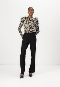 Zwarte bloemenblouse met gerimpelde mouwen, gecombineerd met op maat gemaakte zwarte broek en zwarte pumps met puntige neuzen en decoratieve banden.