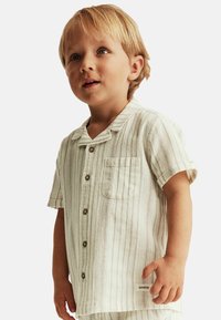 Korte mouw, geknoopte kinderhemd in lichtbeige met verticale strepen, voorzien van een borstzak en knoopsluiting. Zachte textuur.