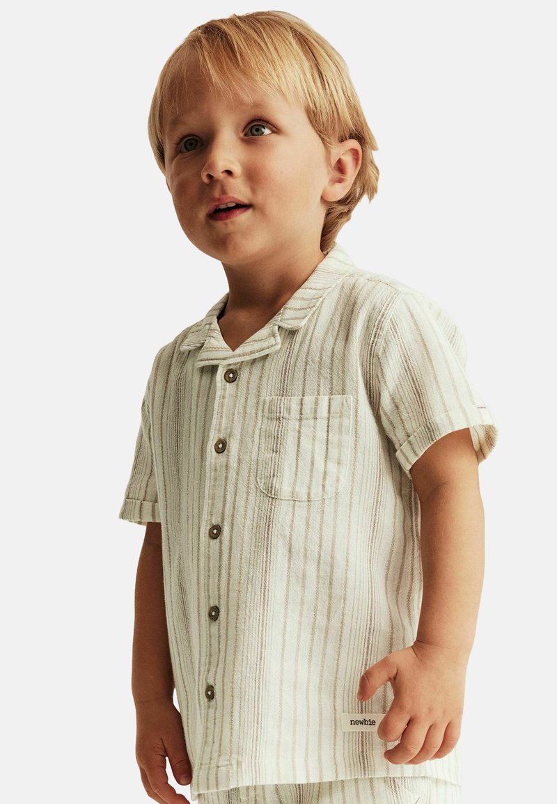 Korte mouw, geknoopte kinderhemd in lichtbeige met verticale strepen, voorzien van een borstzak en knoopsluiting. Zachte textuur.