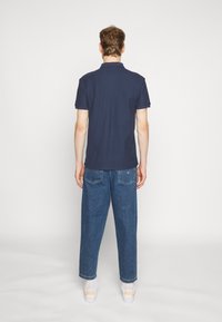 Mörkblå pikétröja med korta ärmar, kombinerad med ljusblå baggyjeans och vita sneakers med orange detaljer.