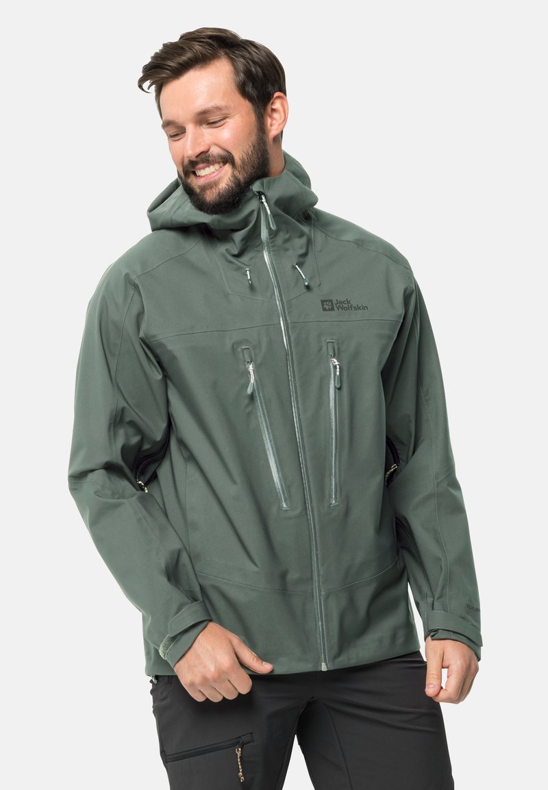 Giacca impermeabile verde realizzata in tessuto liscio, dotata di cappuccio, chiusura frontale con zip e tasche sul petto, polsini regolabili e logo sul petto.