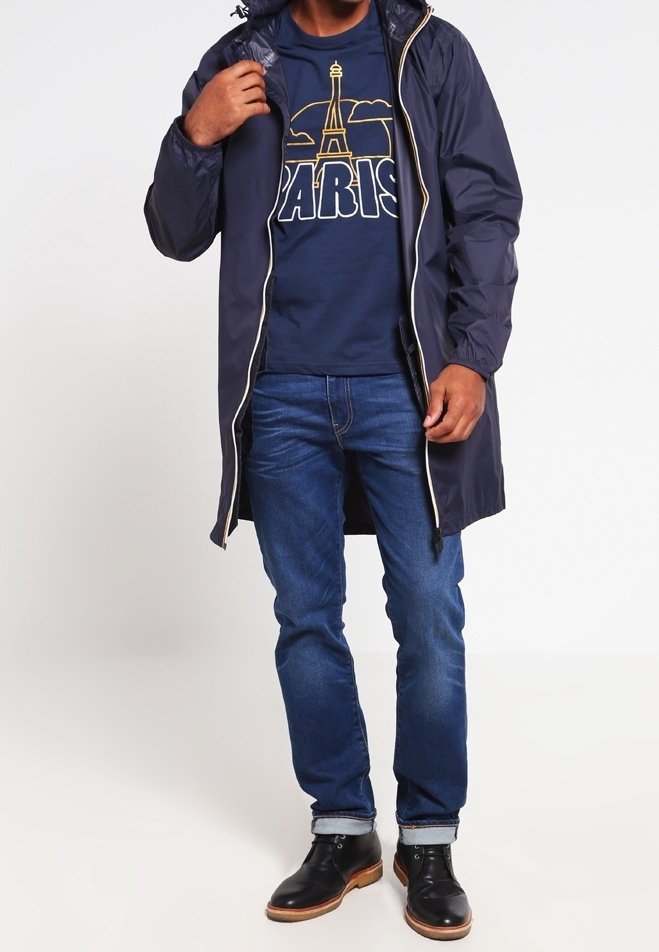 Laivastonsininen vedenpitävä takki, jossa on vetoketjullinen etuosa ja säädettävä huppu, päällä laivastonsininen grafiikkat-paita, jossa on Eiffel-torni, yhdistettynä sinisiin farkkuihin ja mustiin saappaisiin.