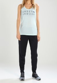 Ljusblå träningstopp med "UNDER ARMOUR" text, tillsammans med svarta joggarbyxor och grå sportskor. Enkelt, atletiskt design och passform.