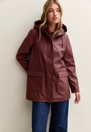 Weinrote wasserdichte Jacke mit Kapuze, Druckknöpfen, zwei vorderen Taschen und einer glatten Textur, kombiniert mit blauen Jeans.