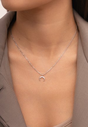Silberne Halskette mit einer filigranen Kette und einem mondförmigen Anhänger, der eine glatte Oberfläche und ein minimales Design aufweist.