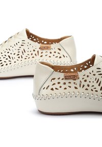 Zapatos de cuero blanco con patrones troquelados, forro interior marrón en contraste y costuras decorativas a lo largo del borde. Marca Pikolinos visible.