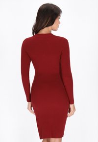 Abito rosso a coste con maniche lunghe e silhouette aderente, che arriva a metà polpaccio. Il tessuto ha un aspetto testurizzato.