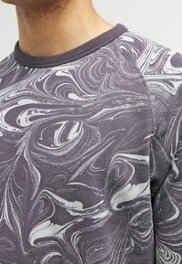 Close-up van een persoon die een grijs en wit gemarmerd shirt met een ronde hals draagt.