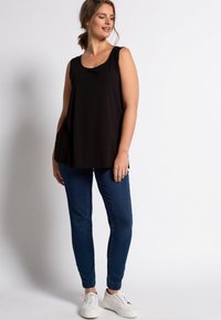 Schwarzes ärmelloses Oberteil mit Rundhalsausschnitt, kombiniert mit dunklen blauen Skinny-Jeans und weißen Sneakers. Glattes Material und lockerer Schnitt.