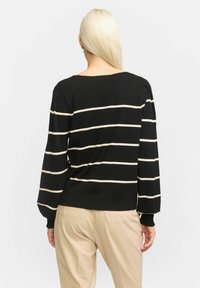 Zwart gestreepte trui met crèmekleurige horizontale lijnen, gemaakt van gebreide stof, heeft een wijde halslijn en geribbelde manchetten, gecombineerd met beige broek.