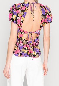 Blouse à imprimé floral avec manches bouffantes, base noire, dos ouvert avec fermeture à nouer, couleurs vives comprenant rose, violet et jaune.