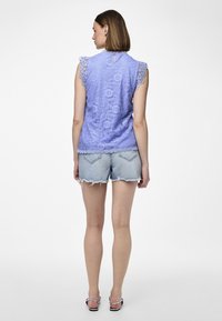 Lavendel blonde topp med bølget ermer og nøkkelhull detalj bak, kombinert med slitte denim shorts, som viser en avslappet sommerstil.